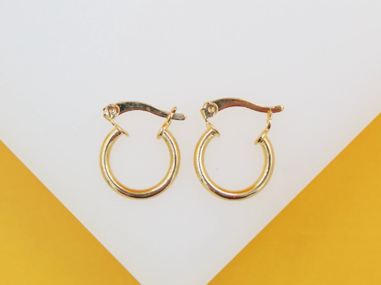 A pair of small gold hoop earrings rests neatly on a white and yellow surface.
