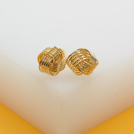 A pair of polished gold knot stud earrings rests on a white display surface.