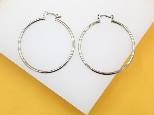 A pair of sleek silver hoop earrings rests on a white display surface against a vibrant orange backdrop.