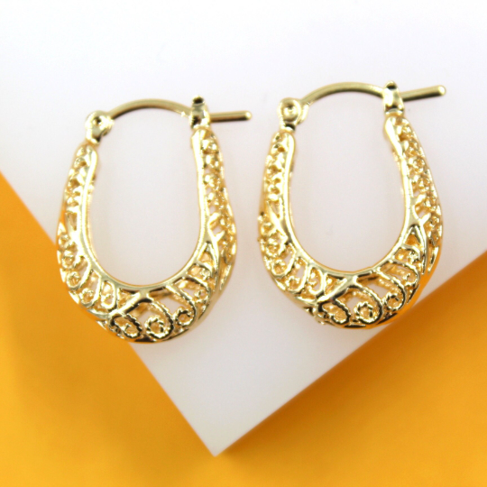 A pair of elegant gold filigree huggie hoop earrings rests against a white and yellow background.