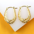 A pair of elegant gold filigree huggie hoop earrings rests against a white and yellow background.