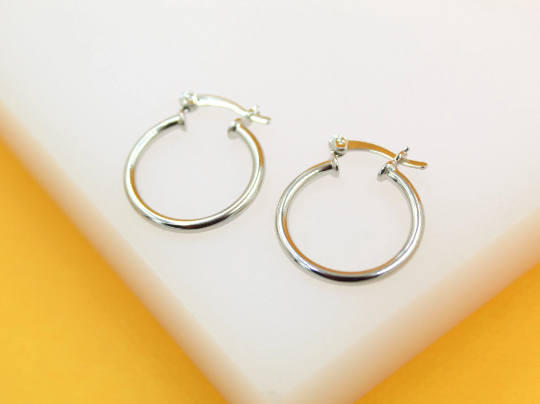 A pair of polished silver hoop earrings rests on a white display surface against a vibrant yellow background.