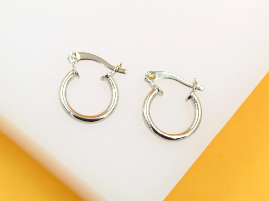 A pair of polished silver small hoop earrings rests on a white and yellow display surface.