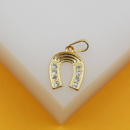 A gleaming gold horseshoe pendant encrusted with sparkling cubic zirconia stones rests on a white display block.