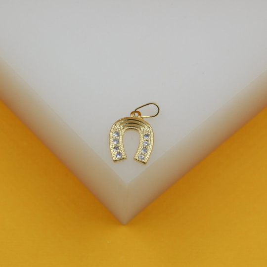A gold horseshoe pendant with sparkling cubic zirconia stones rests on a white display block.