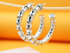 A pair of polished silver spiral hoop earrings hangs from a wooden stick against a bright orange backdrop.