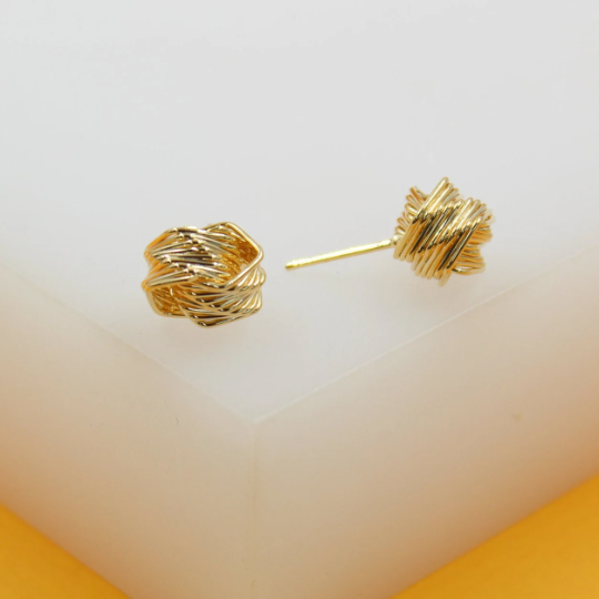 A pair of gold wire-wrapped knot stud earrings rests on a white display surface.