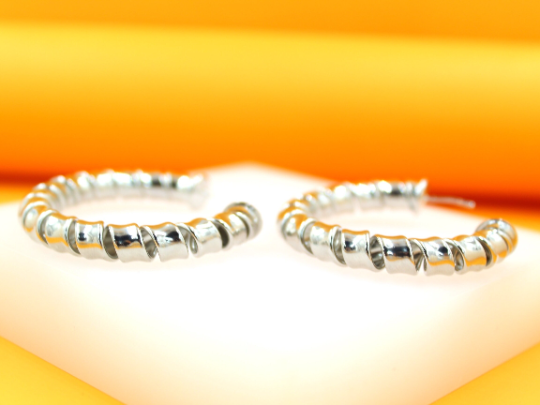 A pair of shiny silver spiral hoop earrings rests on a white platform against a warm yellow background.