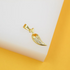 A gold chili pepper pendant embellished with sparkling pave crystals rests on a white display surface against a vibrant yellow background.