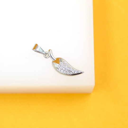 A silver chili pepper pendant embellished with sparkling cubic zirconia rests on a white display block against a vibrant yellow background.