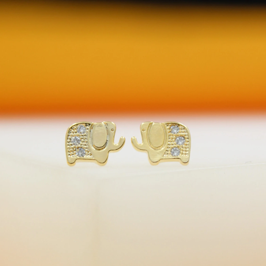 A pair of cute gold elephant stud earrings sparkle against a warm, blurred background.
