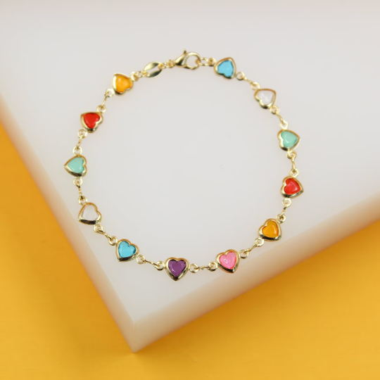 A delicate gold chain bracelet features vibrant, multicolored enamel heart charms displayed on a white and yellow surface.
