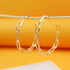 A pair of shiny gold paperclip chain hoop earrings hangs against a vibrant orange background.