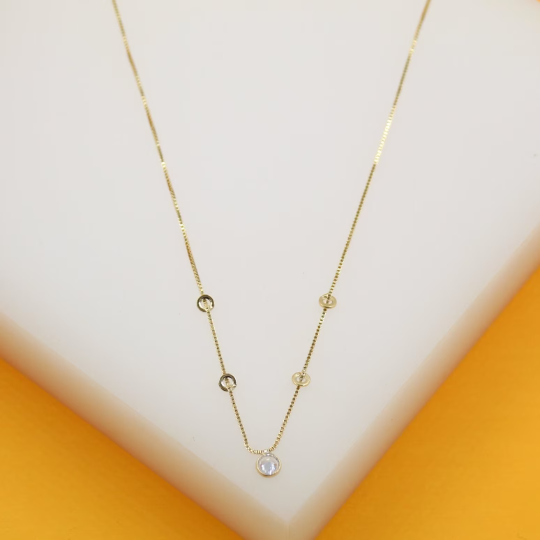 A delicate gold chain necklace featuring small circular accents and a single solitaire pendant rests on a white display surface.
