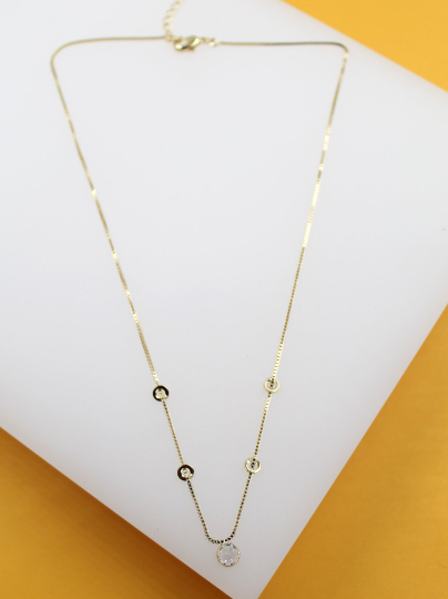 A delicate gold-plated box chain necklace with interspersed circular accents and a sparkling solitaire pendant rests on a white display stand.