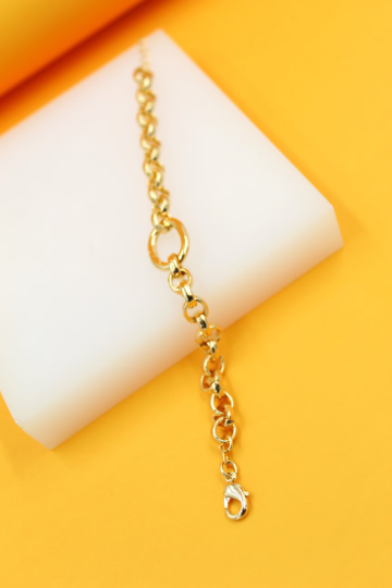 A delicate gold link bracelet rests on a white display block against a vibrant yellow background.