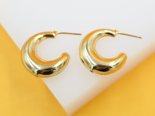 A pair of thick gold hoop earrings rests on a white display against a bright yellow background.