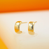 A pair of small, thick gold hoop earrings rest upright on a white display surface against a warm orange background.