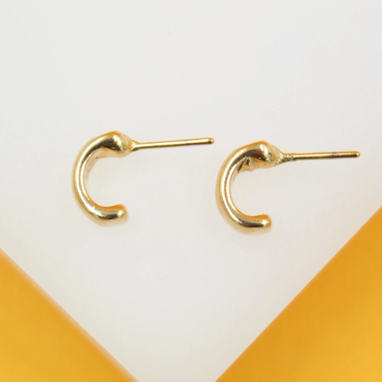 A pair of thick gold C-shaped huggie earrings rests on a light background.
