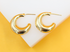 A pair of shiny gold chunky hoop earrings rests on a white and yellow display stand.