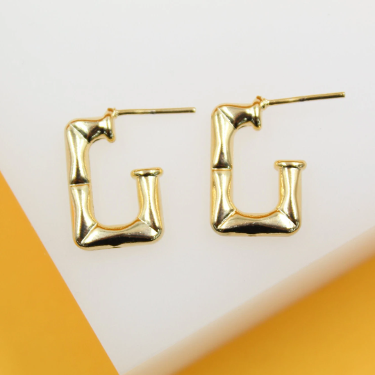 A pair of shiny gold-plated bamboo-textured hoop earrings rests on a white and yellow surface.