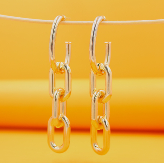 A pair of gold chain-link hoop earrings hangs against a vibrant yellow background.