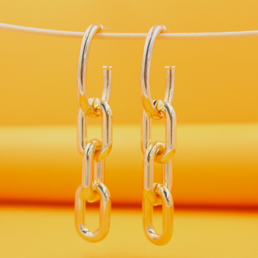 A pair of gold chain-link hoop earrings hangs against a vibrant yellow background.
