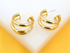 A pair of shiny gold double-hoop earrings rests on a white display stand.