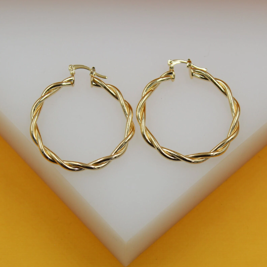 A pair of polished gold twist hoop earrings rests on a white display surface.