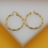 A pair of polished gold twist hoop earrings rests on a white display surface.