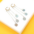A pair of silver hoop earrings with cascading multi-strand chains and dangling coin charms rests on a white display surface against a vibrant yellow background.