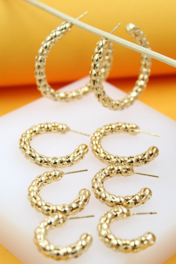 A collection of textured gold hoop earrings displays intricate braided designs in varying sizes against a clean white and yellow background.