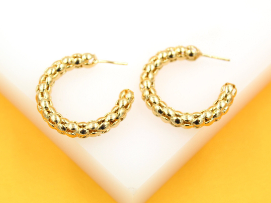 A pair of textured gold hoop earrings rests against a white and yellow background.