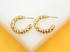 A pair of shiny gold textured hoop earrings rests on a white and yellow display stand.