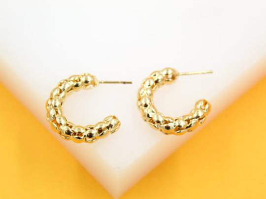 A pair of textured gold hoop earrings rests against a white and yellow background.