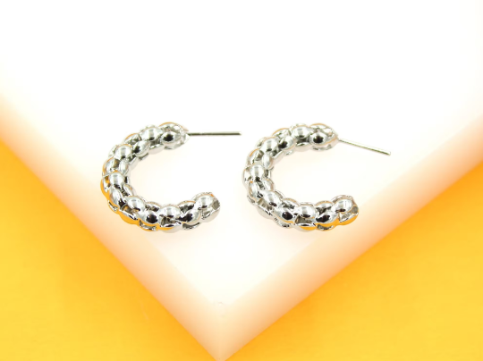 A pair of textured silver hoop earrings rests on a bright white and yellow display stand.