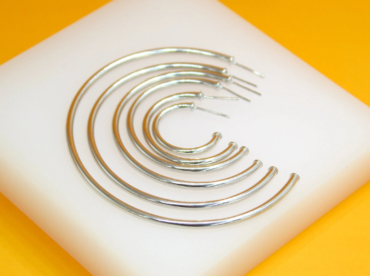 A graduated set of shiny silver hoop earrings rests neatly on a white display surface against a vibrant orange background.