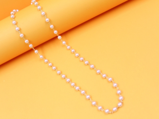 A delicate gold-plated chain adorned with evenly spaced white pearls rests gracefully against a vibrant yellow background.