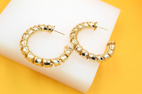 A pair of polished gold spiral hoop earrings rests on a white display block against a vibrant yellow background.
