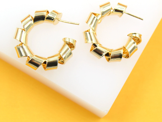 A pair of shiny gold ribbon hoop earrings rests on a white and yellow background.