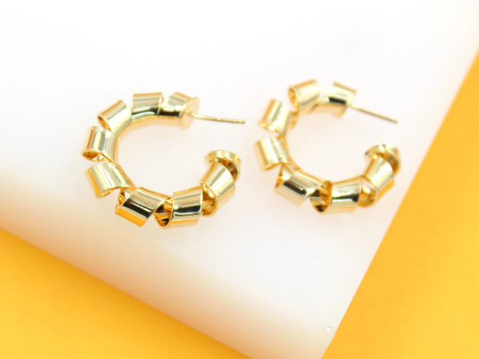 A pair of gold ribbon-wrapped hoop earrings rests on a white and yellow display surface.