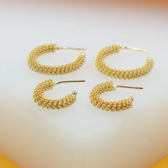 Four textured gold hoop earrings in two different sizes rest on a white surface.