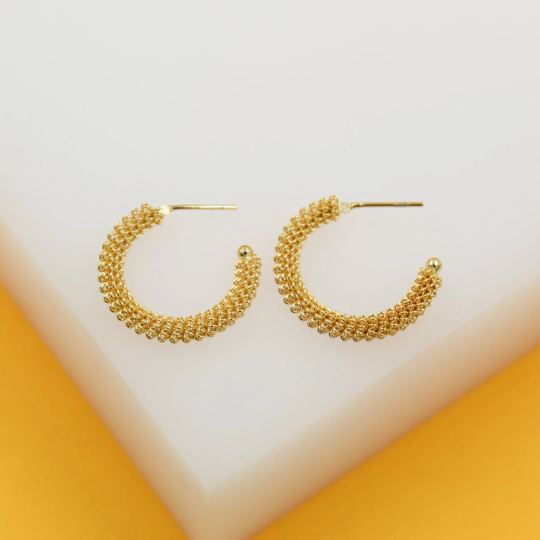 A pair of textured gold hoop earrings rests neatly on a white and yellow display stand.