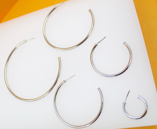 Several sizes of sleek silver hoop earrings display in a graduating arrangement on a white display surface.