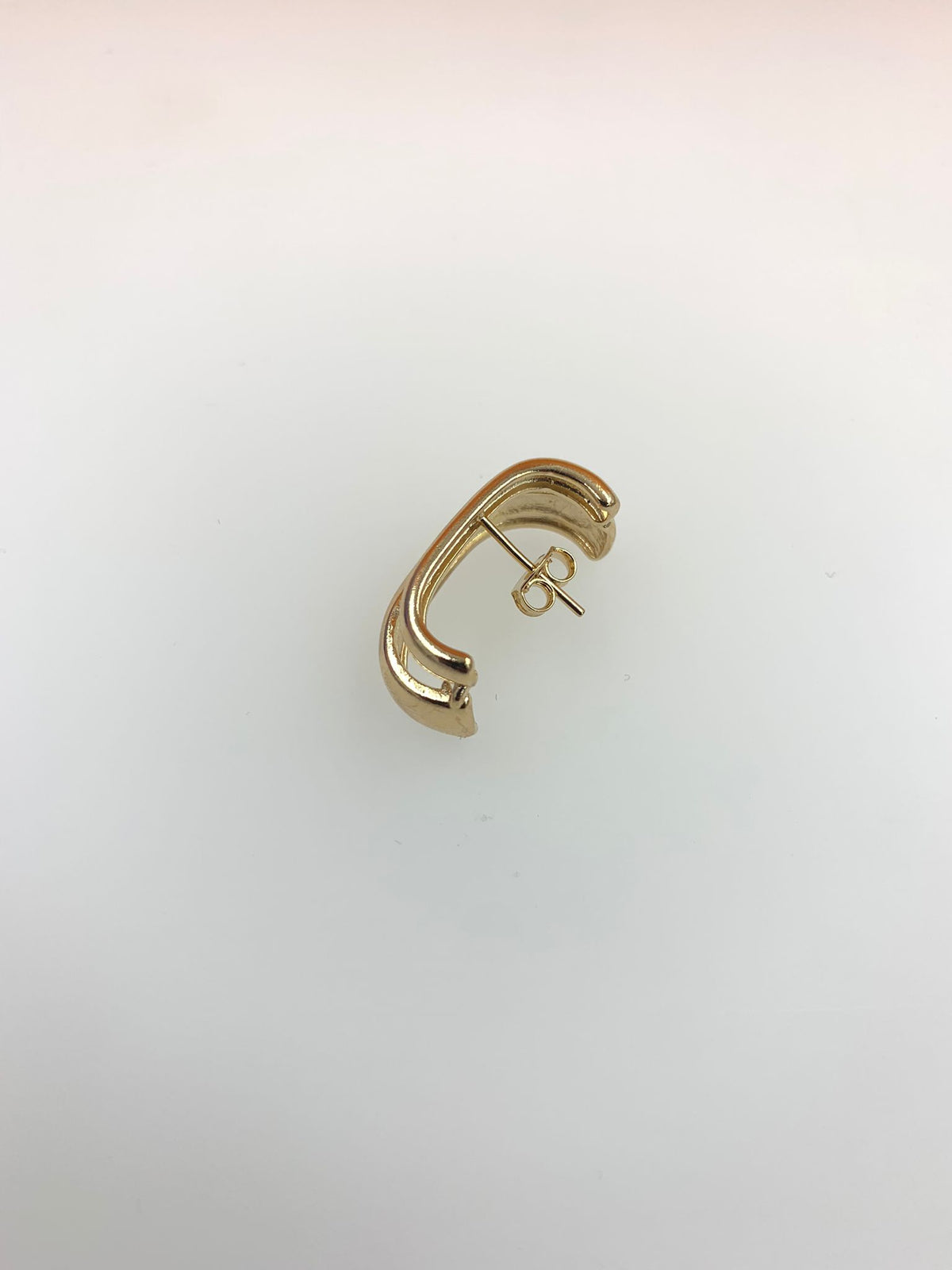 A polished gold double-band stud earring rests against a white background, showcasing its curved geometric design.