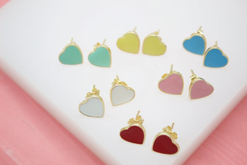 Several pairs of colorful heart-shaped gold stud earrings are arranged on a white display surface.