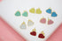 Several pairs of colorful heart-shaped gold stud earrings are arranged on a white display surface.