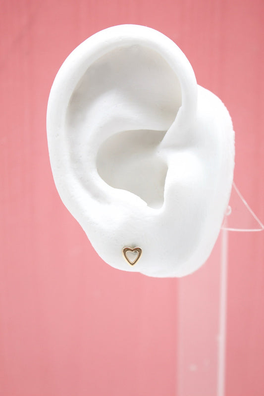 A white display ear model features a dainty gold heart stud earring against a vibrant pink background.