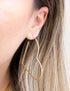 A woman wears a large gold heart-shaped hoop earring in her ear.