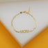 A delicate gold chain bracelet featuring the word "MOM" in block letters rests on a white display surface.